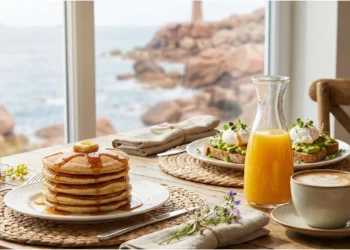Table de brunch garnie de pancakes, jus d'orange et café, avec vue sur la plage en Bretagne.