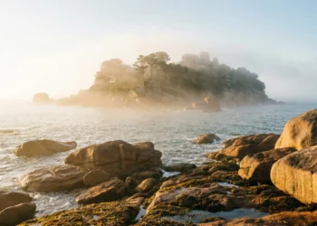 Lever de soleil mystique sur les rochers de la Côte de Granit Rose avec l'Île d'Aval dans la brume, lieu légendaire du repos du Roi Arthur.