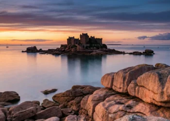 Coucher de soleil flamboyant sur un château au milieu des flots pour des spots romantiques de la Côte de Granit Rose pour la Saint-Valentin.