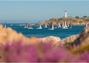 Voilier naviguant en mer devant un phare. La Solitaire du Figaro s'offre un départ à Perros-Guirec en 2026.