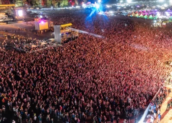 Foule d'un festival de musique, Roi Arthur, en Bretagne dansant devant une grande scène illuminée sous un ciel d'été.