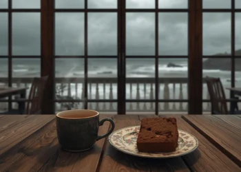 Tasse de thé fumante et pâtisserie bretonne posées sur une table en bois avec vue sur les vagues de la mer en hiver.